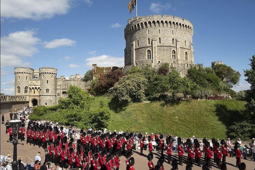 Guards in red tunics and bearskins marching at Windsor Castle with the Round Tower behind them.